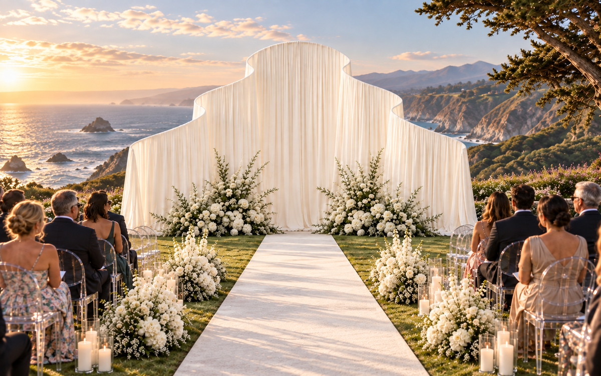 Draped wedding backdrop with floral aisle arrangements at a coastal ceremony